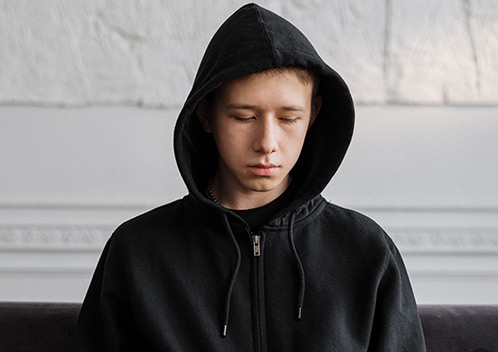 Junge mit schwarzem Kapuzenpulli schaut traurig nach unten